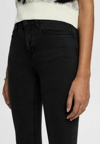 Vaqueros de denim negro con un diseño ajustado, que cuentan con el clásico estilo de cinco bolsillos y detalles de costura sutiles. Textura suave, corte de pierna slim.