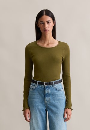 Olijfgroene geribbelde longsleeve top met een ronde halslijn, gecombineerd met lichtblauwe hoog getailleerde jeans en een zwarte riem. Rimpelrand bij de mouwen.