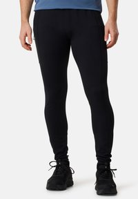 Schwarze Sportleggings mit schmaler Passform, ausgestattet mit seitlichen Reißverschlusstaschen und einer weichen Textur, kombiniert mit schwarzen Sportschuhen.
