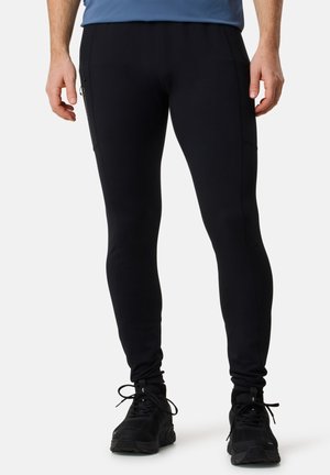 Leggings de sport noirs à coupe slim, dotés de poches zippées sur les côtés et d'une texture douce, associés à des chaussures de sport noires.