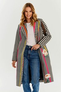 Płaszcz w wzór houndstooth w czarno-białych kolorach, z wyrazistymi akcentami w różowym, pomarańczowym i żółtym, z kwiatowymi detalami. Długie rękawy i długość do kolan.