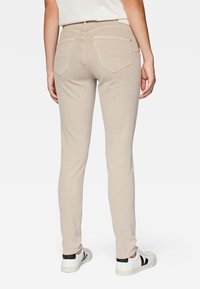 Beige skinny jeans made of cotton blend, featuring a standard waistband, back pockets, and worn with white sneakers.