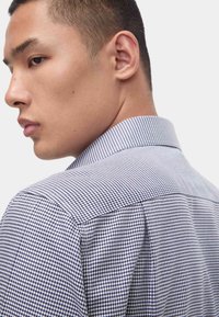 Camicia da uomo con motivo a quadri blu e bianchi, colletto button-down e tessuto liscio, caratterizzata da una vestibilità su misura e spalle strutturate.