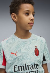 Maglia da calcio azzurra chiara con un motivo testurizzato, dettagli rossi, logo Puma e stemma dell'AC Milan sul petto. Maniche corte, collo rotondo.