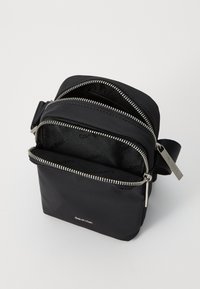 Černá nylonová crossbody taška s více zipovými přihrádkami, stříbrnými kovovými doplňky a značkovou podšívkou. Hladký povrch po celém obvodu.