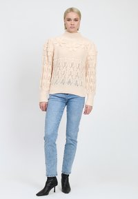 Maglione lavorato a maglia color pesca chiaro con dettagli floreali, maniche con motivo e orlo a coste, abbinato a jeans blu e stivaletti neri con tacco.