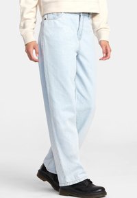 Světle modré džíny s rovnými nohavicemi, vysokým pasem, pětifunkčním designem a prošitými detaily. Kombinované s černými botami.