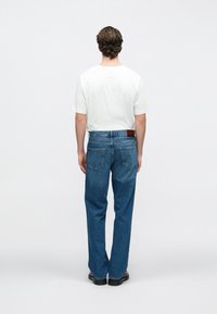 Μπλε τζιν παντελόνια με ίσια γραμμή, πέντε τσέπες και καφέ δερμάτινη λεπτομέρεια στη πίσω ζώνη. Συνδυασμένα με λευκό μπλουζάκι.