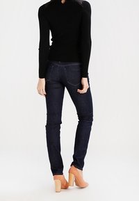 Tmavě modré džíny s hladkou texturou, doplněné černým žebrovaným topem s krajkovými detaily na ramenech. Světlé boty na blokovém podpatku.