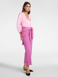 Rosa Satin-Langarmtop, rosa taillierte Hose mit Bünden und braunen Slingback-Absätzen. Auffällige Merkmale sind ein V-Ausschnitt und ein gebundener Pullover.
