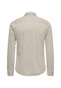 Camisa de manga larga beige con cuello clásico, puños abotonados y una textura suave. Presenta un diseño trasero limpio y minimalista.