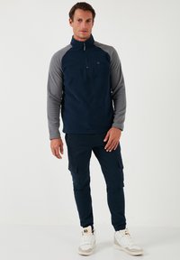 Navy fleece pullover with gray sleeves, half-zip collar, and subtle logo. Paired with navy cargo pants and white high-top sneakers.