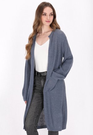 Cardigan lungo aperto davanti in un morbido knit blu testurizzato con maniche lunghe e tasche laterali, abbinato a una maglietta bianca e jeans scuri.