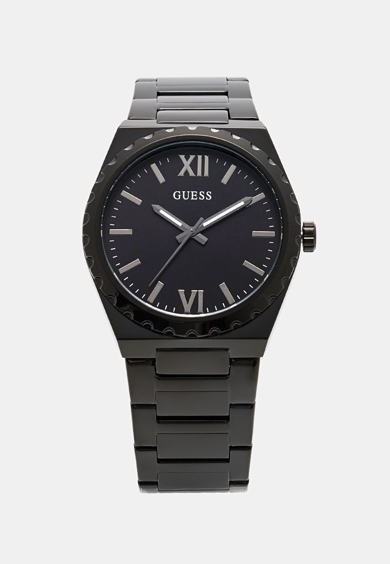 Schwarze Metall-Uhr von Guess mit rundem Ziffernblatt, römischen Ziffern bei 12 und 6 Uhr sowie einem eleganten Armband mit gestapelten Gliedern.