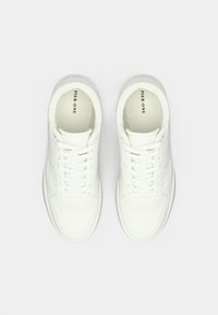 Λευκά αθλητικά παπούτσια με λείο δερμάτινο φινίρισμα, στρογγυλή μύτη, περφοραρισμένες λεπτομέρειες, επίπεδες κορδόνες και απλό, μινιμαλιστικό σχεδιασμό.