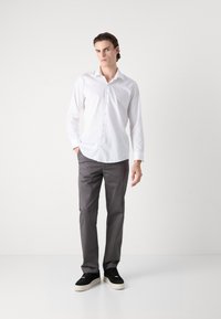 Vit långärmad skjorta med rak skärning, kombinerad med grå byxor och svarta sneakers. Minimalistisk design, mjuk tygtextur.