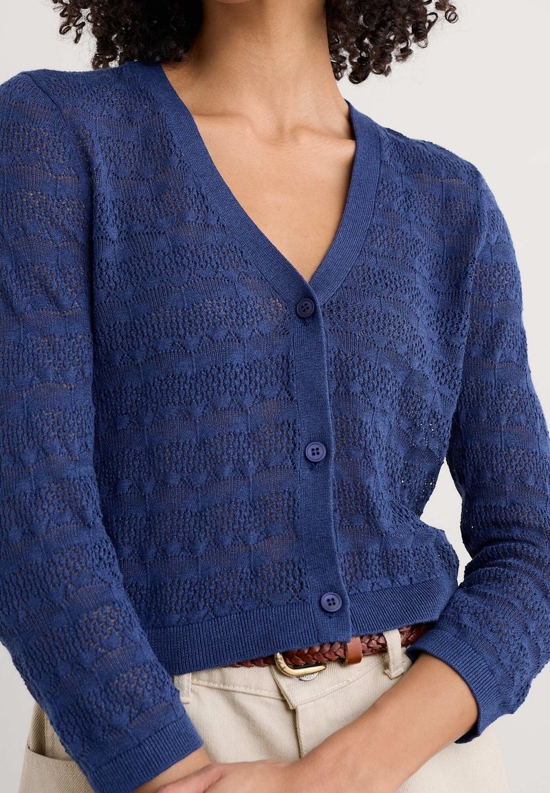 Marineblauer Cardigan mit V-Ausschnitt, gestricktem Muster und Knopfverschluss. Der Stoff wirkt leicht und strukturiert und hat einen gerippten Saum.