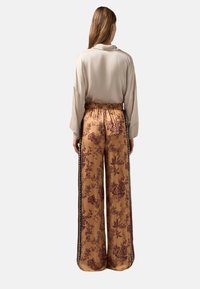 Beige blouse met brede mouwen, gecombineerd met losse, bloemenpatroon mosterdkleurige broek met zijstrepen en een elastische tailleband.