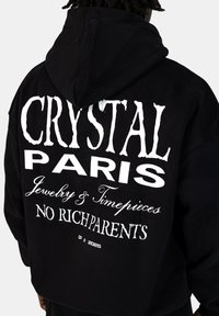 Felpa nera con cappuccio che presenta un grande testo bianco sul retro: "CRYSTAL PARIS Jewelry & Timepieces NO RICH PARENTS," con una finitura in tessuto testurizzato.