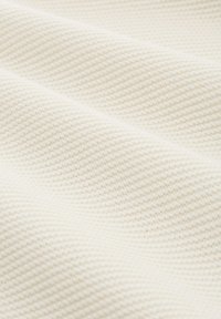 Close-up van zacht, roomkleurig gebreid stof met een licht gewatteerd patroon en zachte plooien.