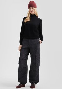 Maglione nero a collo alto, pantaloni cargo in stampa leopardo grigio scuro e berretto a maglia bordeaux, abbinati a scarpe basse rosso scuro.