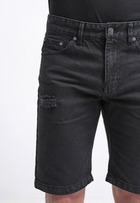 Svarta denimshorts med en sliten detalj på vänster lår, femfickorsdesign, knappstängning och rak benpassform.