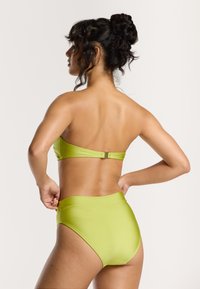 Lime žalia bikinio rinkinys, turintis bandeau tipo liemenėlę su užsegimu gale ir aukštu liemeniu kelnių dalimi, abi dalys pagamintos iš lygaus, blizgaus audinio.