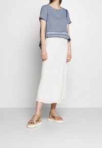 Blå mönstrad kortärmad topp med vit texturerad maxikjol och tanfärgade platåsandaler med vävda detaljer och justerbara remmar.