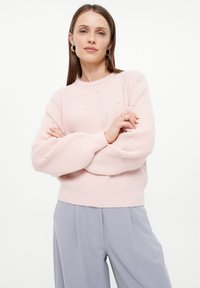 Hellrosa Rippstrickpullover mit Perlenverzierungen und Rundhalsausschnitt. Weicher Stoff mit entspannten, ballonförmigen Ärmeln.