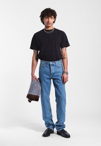 Černé bavlněné tričko, světle modré džíny s vysokým pasem, stříbrné šperky, držící šedohnědý vzorovaný pletený svetr. Černé kožené boty.