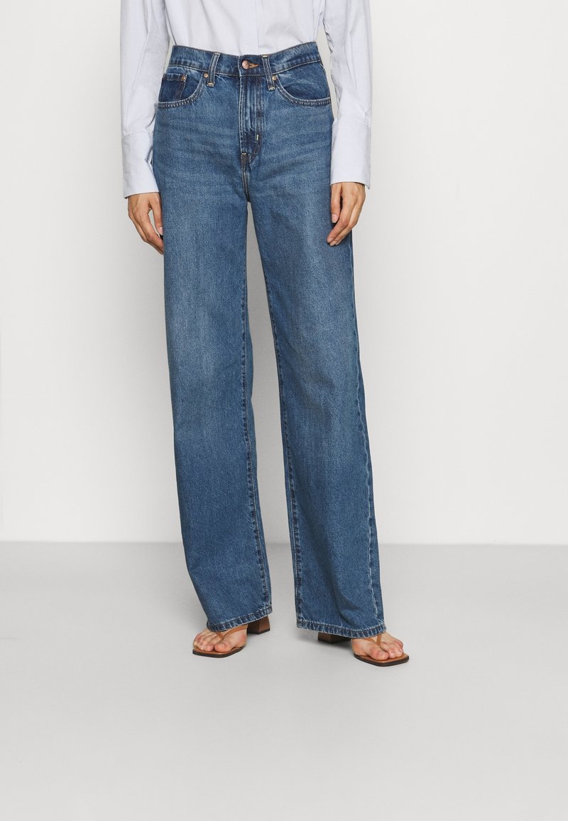 Široké džíny ve středně modré denimové barvě, s vysokým pasem, předními kapsami a klasickým zapínáním na knoflík. Měkká textura, minimální opotřebení.