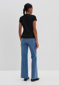 Zwarte t-shirt met korte mouwen, gecombineerd met lichtblauwe uitlopende jeans. Glad materiaal met een aansluitende pasvorm, voorzien van een eenvoudige halslijn en rugdetail.