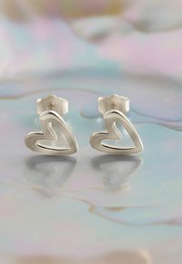 Boucles d'oreilles en argent en forme de cœur avec un design intérieur ouvert et un dos texturé pour un maintien sécurisé. Surface réfléchissante sur un fond doux.