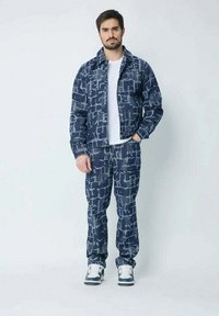 Veste et pantalon bleu marine avec un motif abstrait texturé. T-shirt blanc en dessous. Baskets décontractées complètent la tenue.
