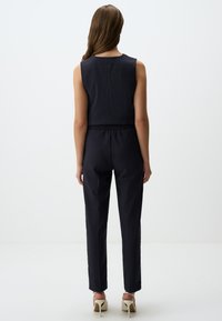 Navyblauwe jumpsuit met verticale streepjes, mouwloos ontwerp, elastische tailleband, taps toelopende benen en minimalistische stijl.