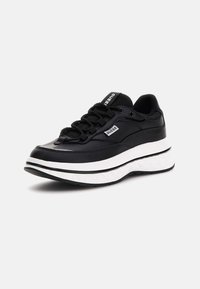 Sneaker sportive nere con finitura lucida, caratterizzate da una suola intermedia bianca e testurizzata, design con lacci e un piccolo logo sul lato.