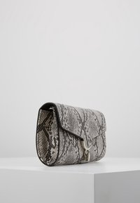 Clutch taška s hadím vzorem v černé a bílé barvě, se zavíráním na klapku a stříbrnými kovovými detaily. Texturovaný povrch dodává na zajímavosti.