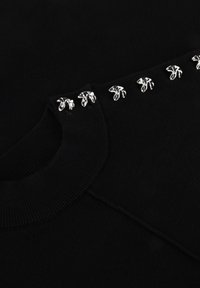 Zwarte trui met een getextureerde gebreide kraag en zilveren bloemmotieven langs de schouder. Glad materiaal met een aansluitende pasvorm.