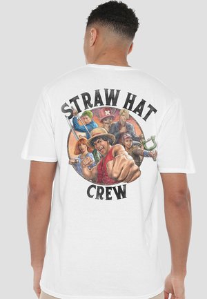 Mann trägt ein weißes T-Shirt mit bunten Anime-Figuren der "Straw Hat Crew", eine Person zeigt mit dynamischer Pose nach vorne auf dem Rücken.