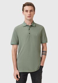 Polo shirt in cotone verde con colletto, pattina a due bottoni, maniche corte e un piccolo logo ricamato sul petto.