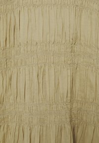 Ljust beige tyg med samlad struktur och horisontella sömmar som skapar en serie vertikala plisseringar genom hela materialet.