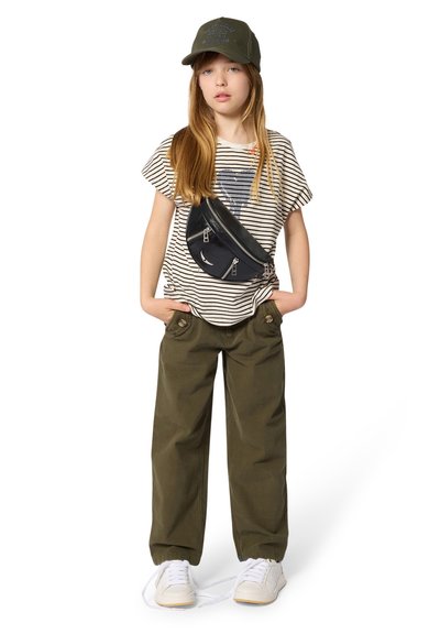T-shirt rayé avec motif cœur, pantalon vert olive avec détails à boutons, sac bandoulière noir et casquette de baseball olive. Baskets blanches à lacets.