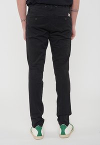 Pantaloni neri con un design aderente, due tasche posteriori con bottoni e una trama liscia. Abbinati a sneakers verdi e bianche.