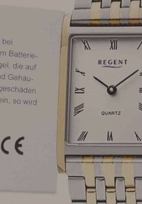 Montre en quartz rectangulaire argentée et dorée avec des chiffres romains, des aiguilles noires et un bracelet texturé ; comprend une étiquette d'instructions d'entretien.