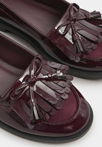 Burgundyröda lackskor med fransdetaljer och en rosettaccent. Har en strukturerad innersula och slät yttersida, med en svart gummisula.