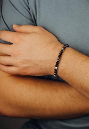 Black bead bracelet with silver accents on a wrist, showcasing a smooth texture and round shapes. Hand resting on a bare arm.