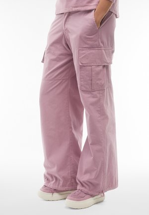 Rosa Cargo-Hosen aus leichtem Stoff, mit großen seitlichen Taschen, einer lockeren Passform und umgeschlagenen Säumen, kombiniert mit pastellfarbenen Schuhen.
