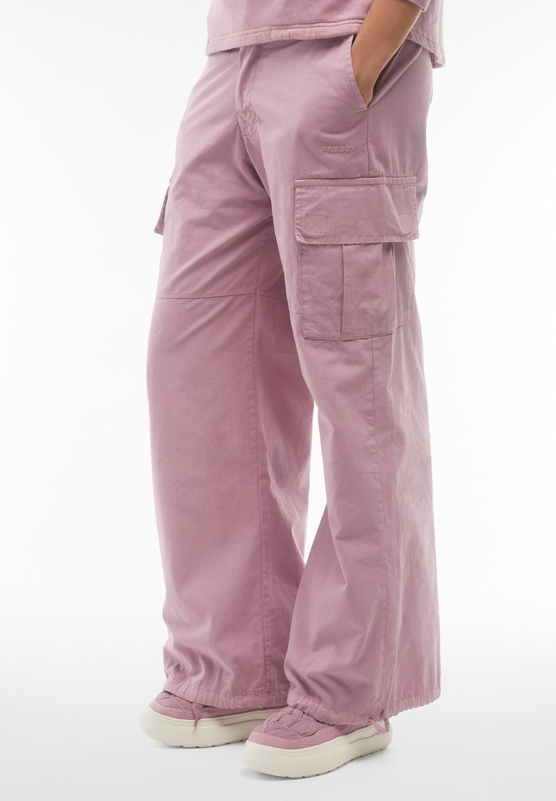 Pantaloni cargo rosa realizzati in tessuto leggero, con ampie tasche laterali, una vestibilità rilassata e orli a costine abbinati a scarpe pastello.