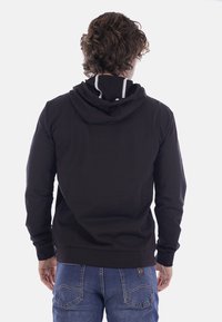 Felpa nera con cappuccio e corsetto, polsini e orlo a coste, con una fodera interna a contrasto sul collo. Mostrata da dietro.
