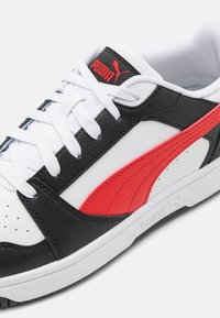 PUMA sneakers har sort tekstureret læder, hvide paneler og et slående rødt sidebånd. Inkluderer hvide snørebånd og en gummisål.